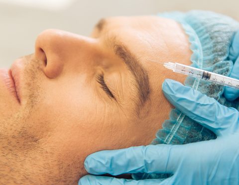 Side view of handsome young man getting an injection in face, lying with closed eyes, close-up