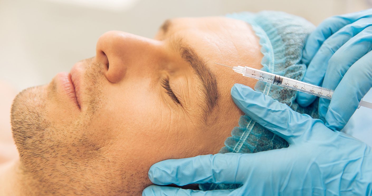 Side view of handsome young man getting an injection in face, lying with closed eyes, close-up