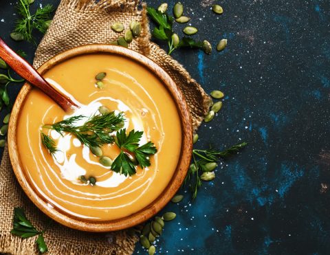 Creamy pumpkin soup in a wooden bowl, blue background, top view